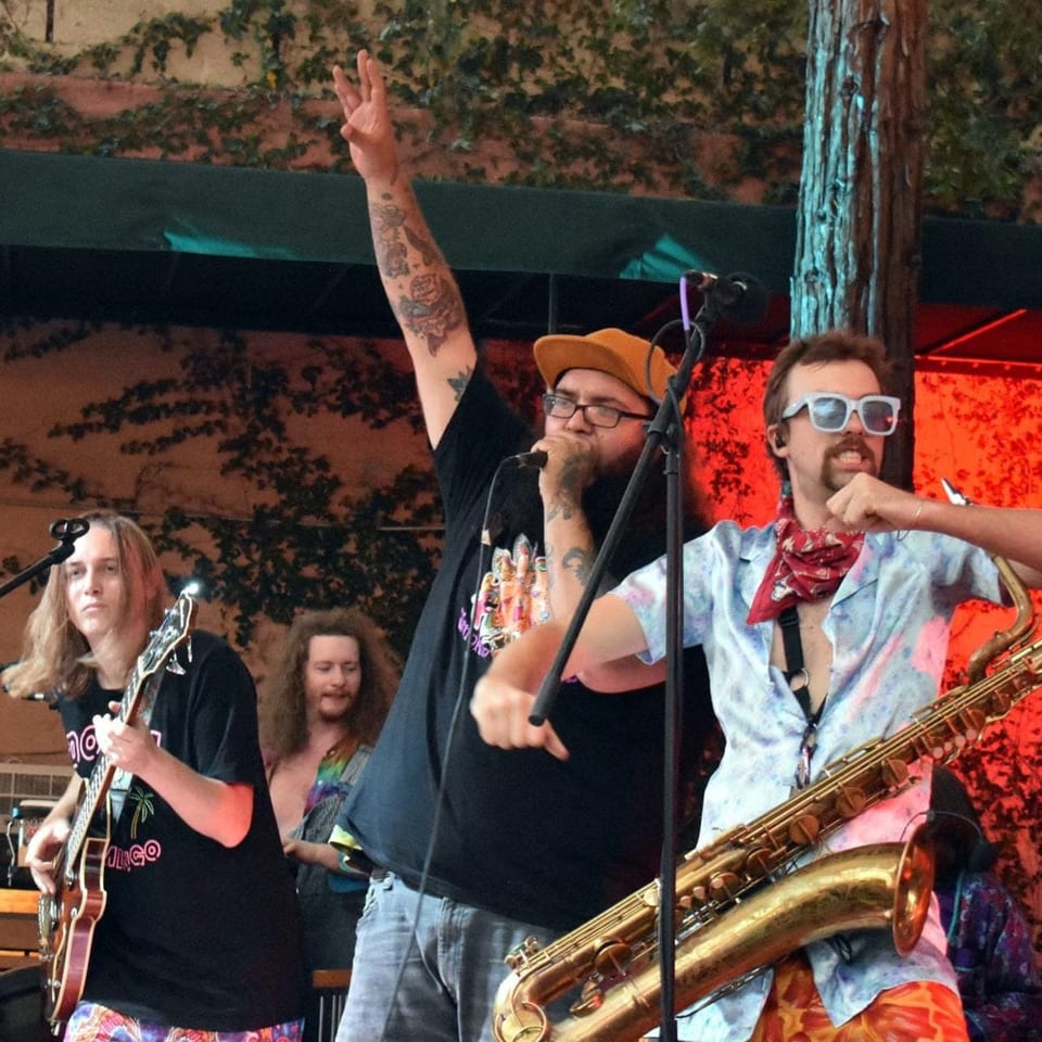 A band performs live, with a singer, guitarist, and saxophonist on stage.