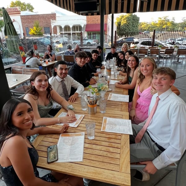 A group of young adults in formal attire smiling at a long table on Union's outdoor patio.