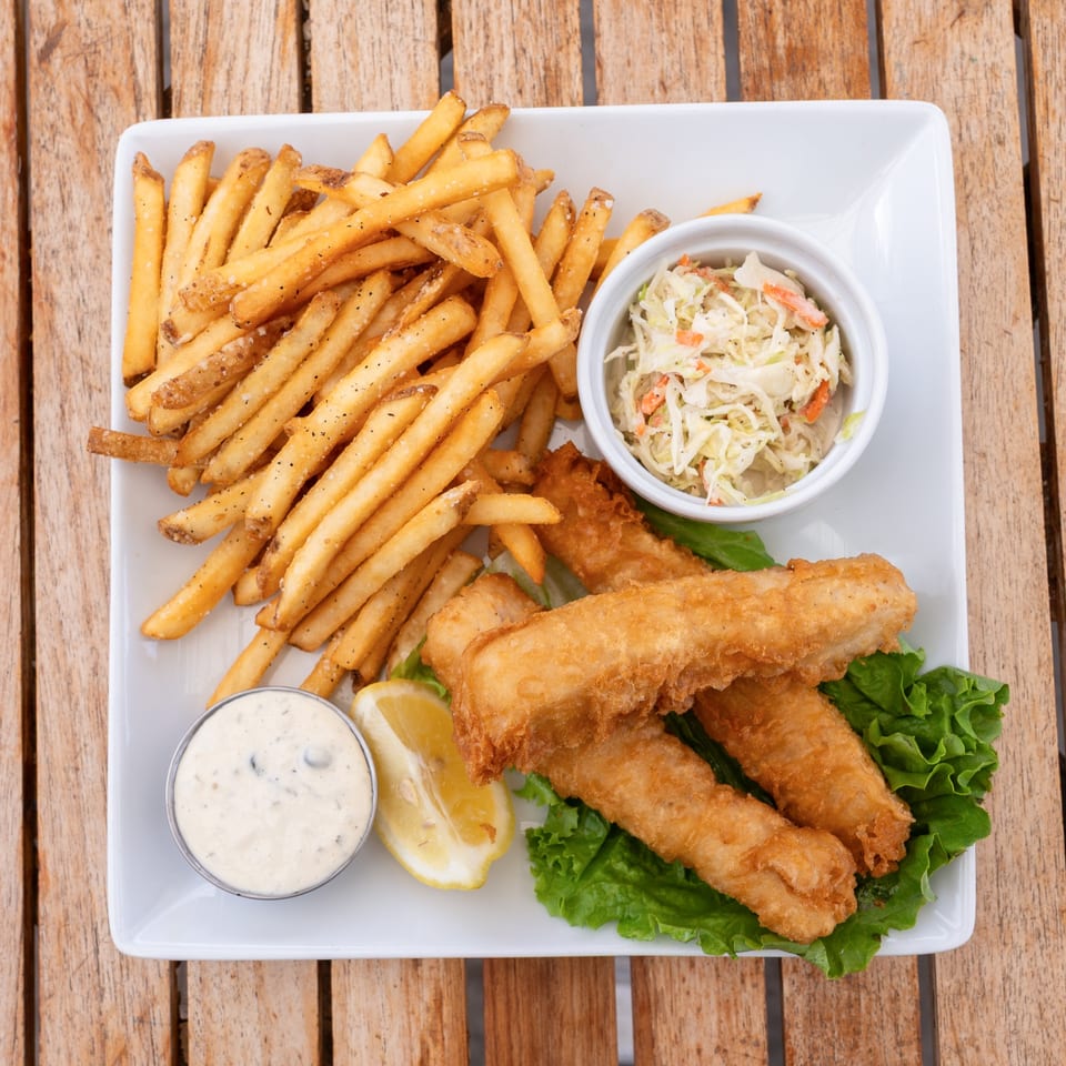 A white plate of golden fish and chips with coleslaw, tartar sauce, and a lemon wedge.