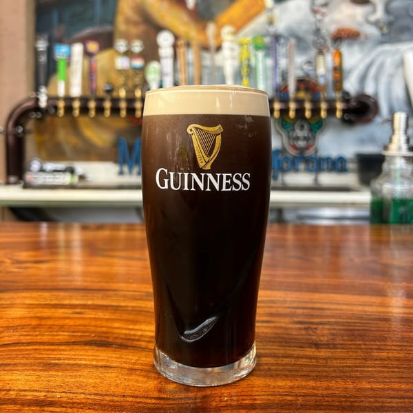 A pint of Guinness beer with a creamy head sits on a wooden bar top.