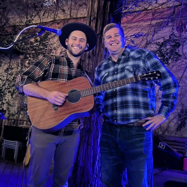 Two men, one playing guitar, smiling under blue lights at Union restaurant.