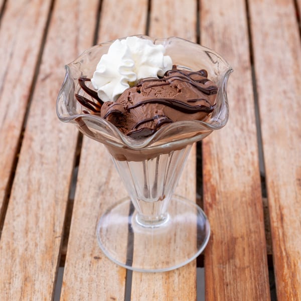 Chocolate ice cream with chocolate syrup and whipped cream in a glass dish on a wooden table.