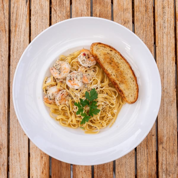 Shrimp scampi with linguine, parmesan, parsley, and garlic bread on a white plate.