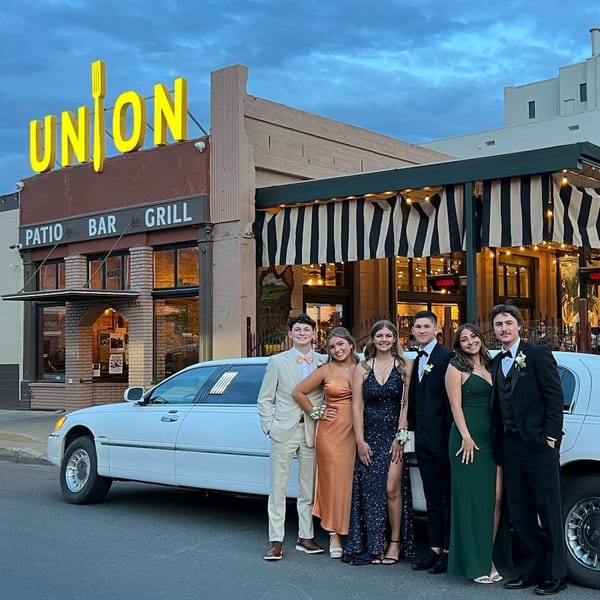 Six young adults in formal wear pose in front of Union restaurant with a white limousine.