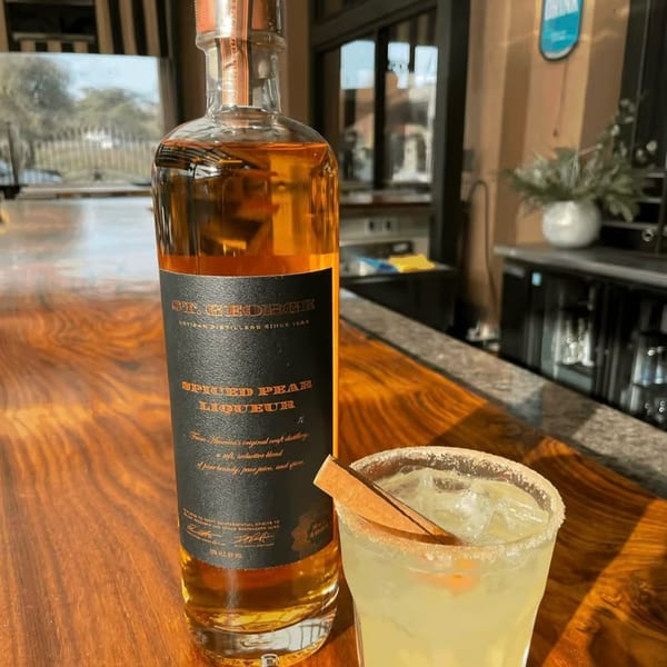 A bottle of St. George Spiced Pear Liqueur next to a cocktail with a cinnamon stick.