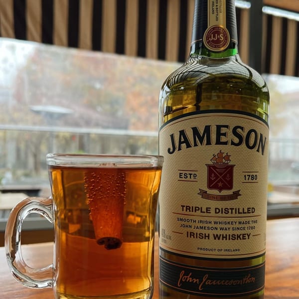 A glass of amber liquid with a cinnamon stick next to a bottle of Jameson Irish Whiskey.