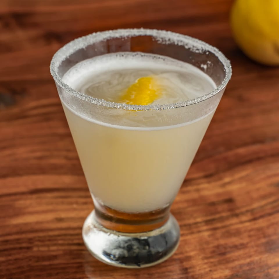 A Union restaurant cocktail, light yellow with a sugared rim and lemon peel garnish, on a wooden table.