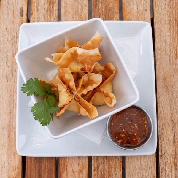 Crispy crab rangoon in a white bowl with a side of dipping sauce and cilantro garnish.