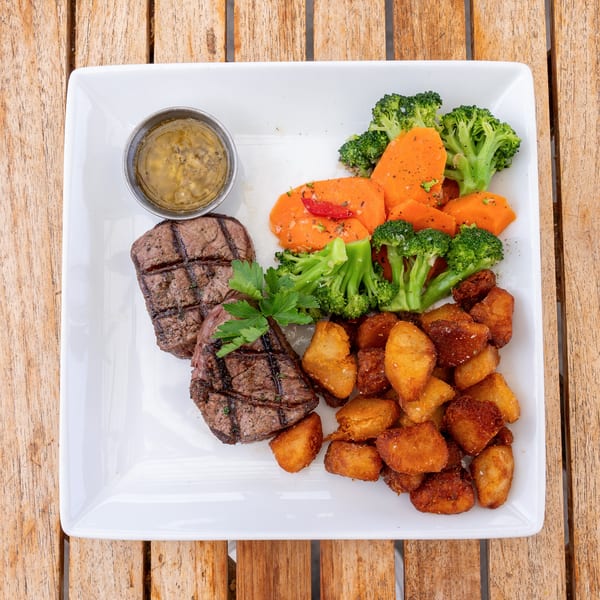Grilled steak medallions with roasted potatoes, broccoli, sweet potatoes, and a side of sauce.