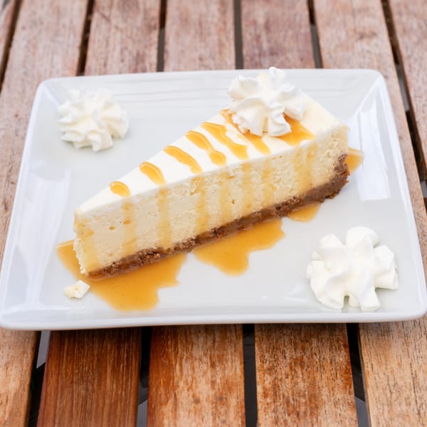 Slice of cheesecake with caramel drizzle and whipped cream on a white rectangular plate.