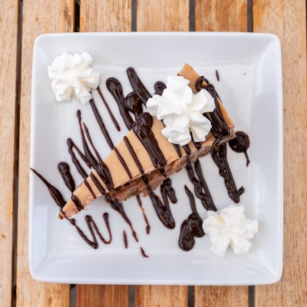 A slice of peanut butter pie with chocolate drizzle and whipped cream on a white plate.