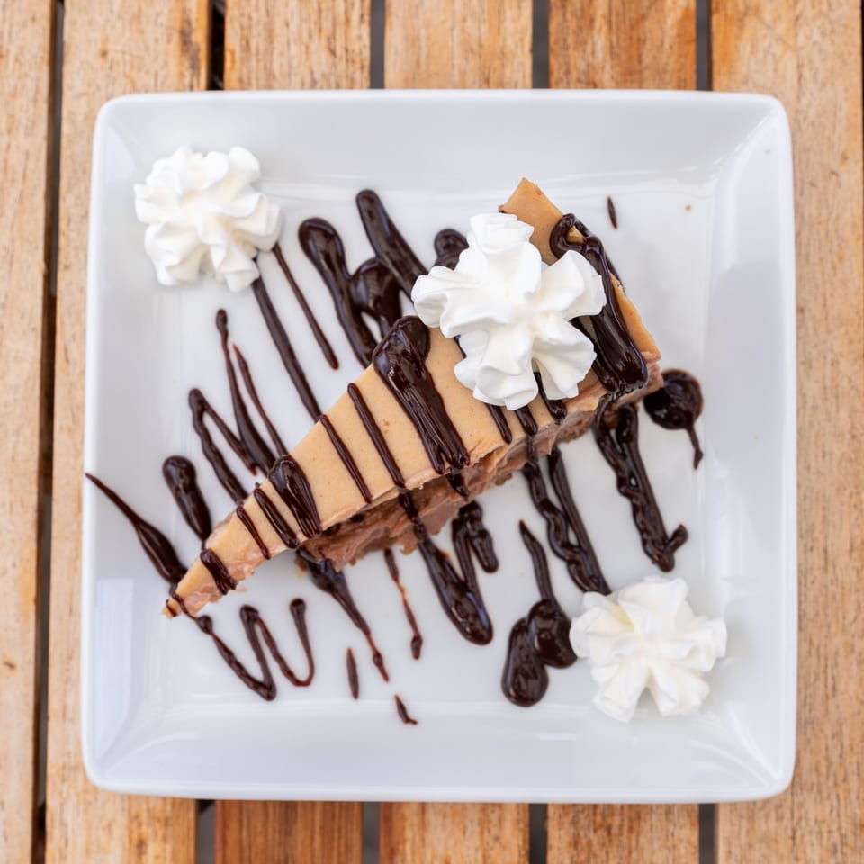 A slice of peanut butter pie with chocolate drizzle and whipped cream on a white plate.
