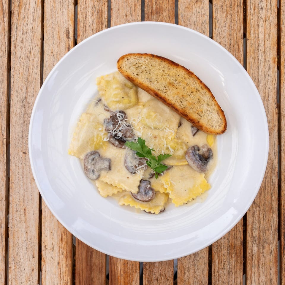 Ravioli with creamy mushroom sauce, garnished with parsley and grated cheese, served with garlic bread.
