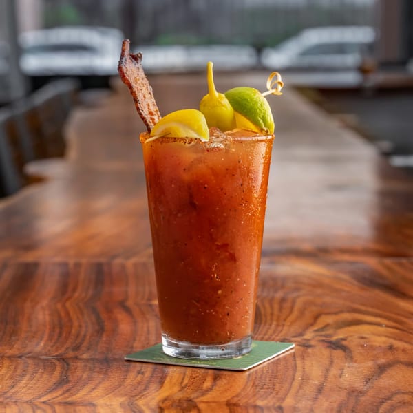 A Union Bloody Mary cocktail with bacon, lemon, lime, and pepper garnish on a wooden table.