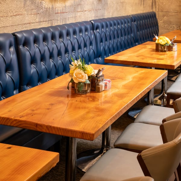 Restaurant interior with blue tufted booths, light wooden tables, and light gray chairs.