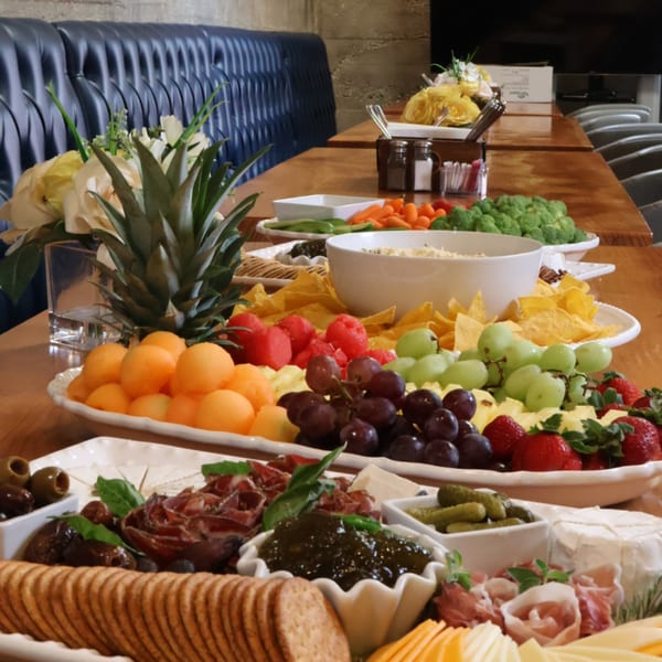 A long wooden table laden with platters of fruit, vegetables, chips, dips, cheeses, and cured meats.