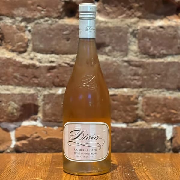 A bottle of Diora La Belle Fête Rosé de Pinot Noir wine on a wooden surface against a brick wall.