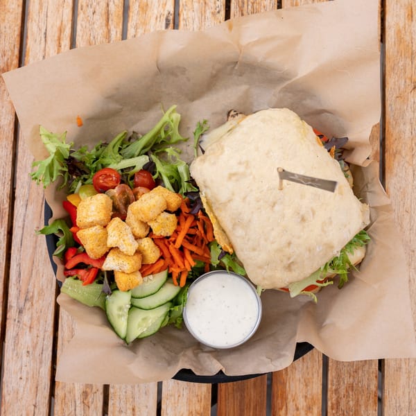Overhead view of a sandwich and side salad with dressing on a wooden table.