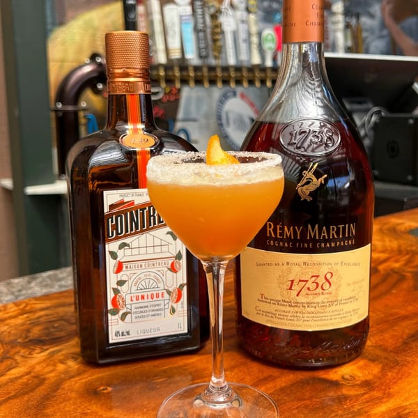 A cocktail with an orange slice and sugar rim, flanked by bottles of Cointreau and Rémy Martin.