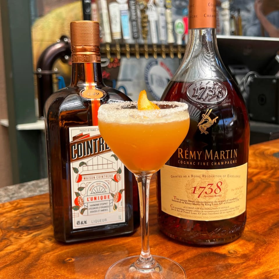 A cocktail with an orange slice and sugar rim, flanked by bottles of Cointreau and Rémy Martin.