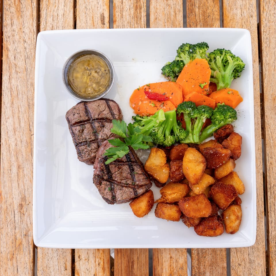Grilled steak with roasted potatoes, broccoli, and sweet potatoes, served with a side of sauce.