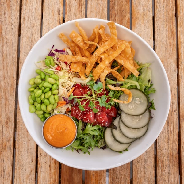 Overhead view of a colorful poke bowl with tuna, edamame, cucumbers, crispy noodles, and sauce.