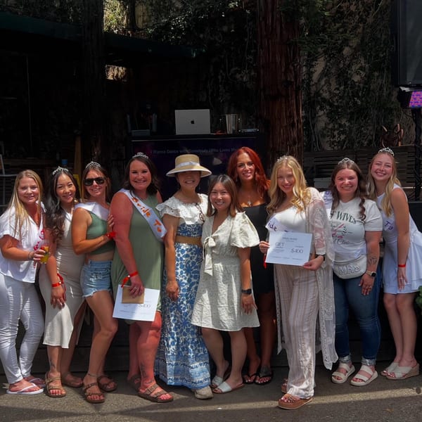Ten women, some wearing tiaras and sashes, pose outdoors with gift certificates at Union.
