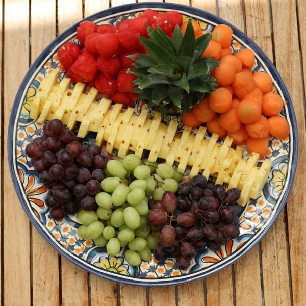 Colorful fruit platter with watermelon, pineapple, cantaloupe, and grapes on a decorative plate.