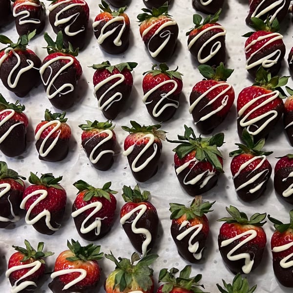 Rows of chocolate-dipped strawberries with white icing swirls on a white surface.