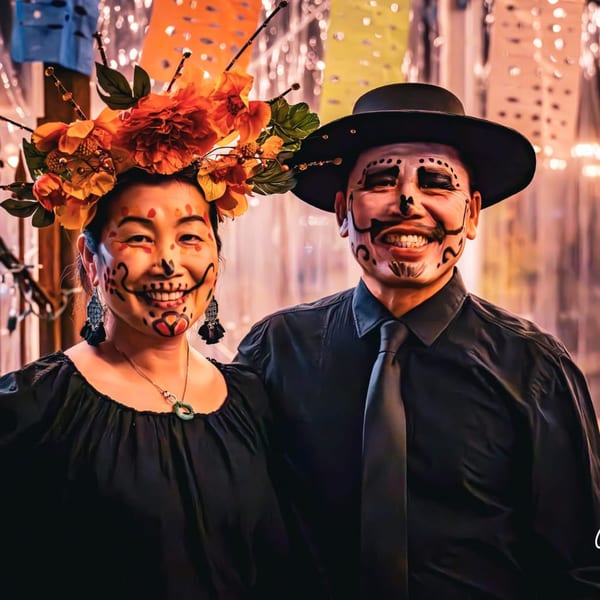 A smiling couple with Day of the Dead face paint, the woman wearing a floral headpiece.