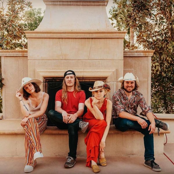 Four people, two men and two women, sitting on a stone bench in front of a fireplace.
