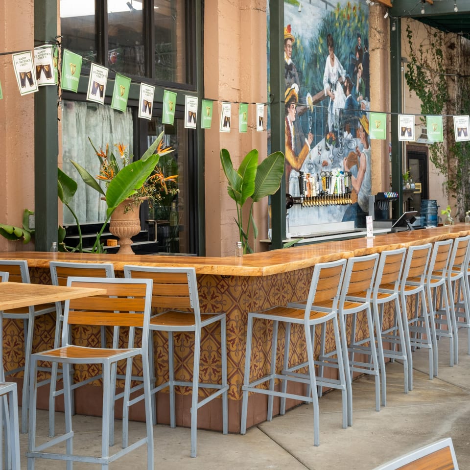 Outdoor bar with St. Patrick's Day decorations, bar stools, and a mural on the wall.