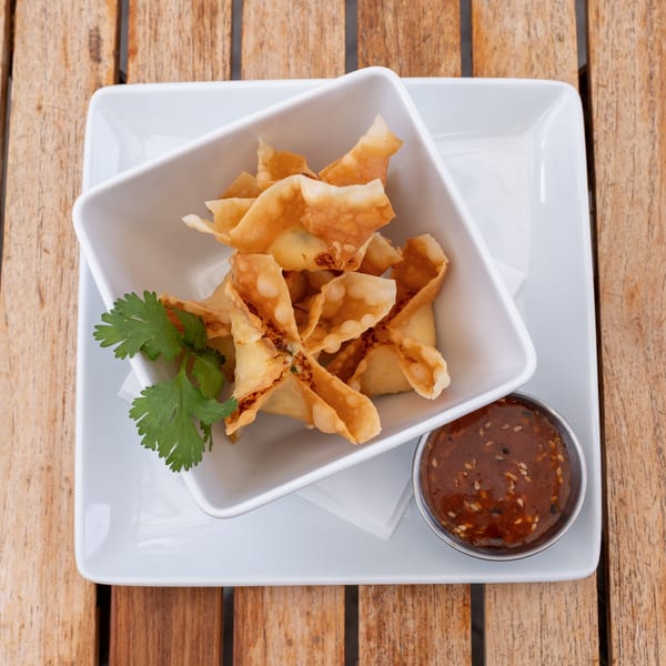 Crispy crab rangoon in a white bowl with cilantro and a side of dipping sauce.