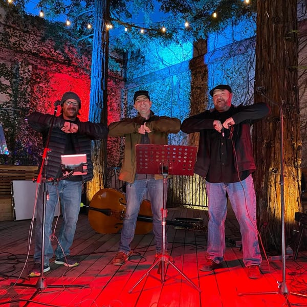 Three men on a stage with red and blue lighting, performing with musical instruments.
