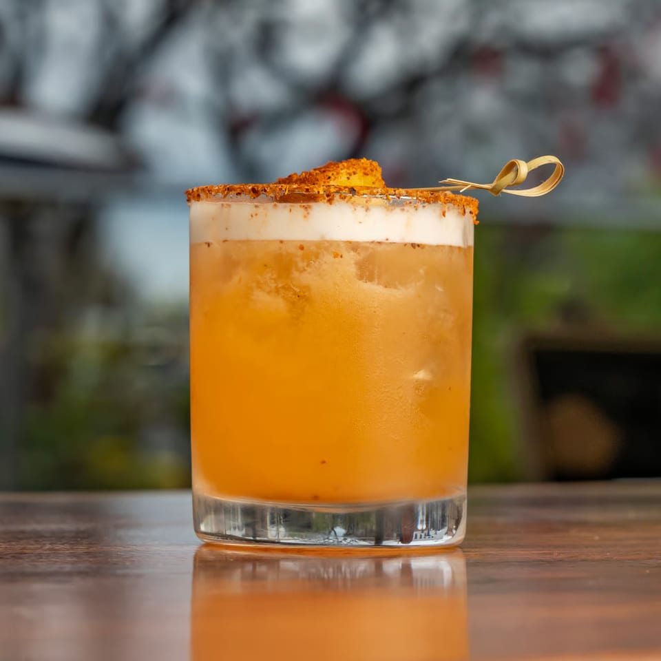 A Union cocktail with a foamy top, spiced rim, and a small garnish on a wooden table.