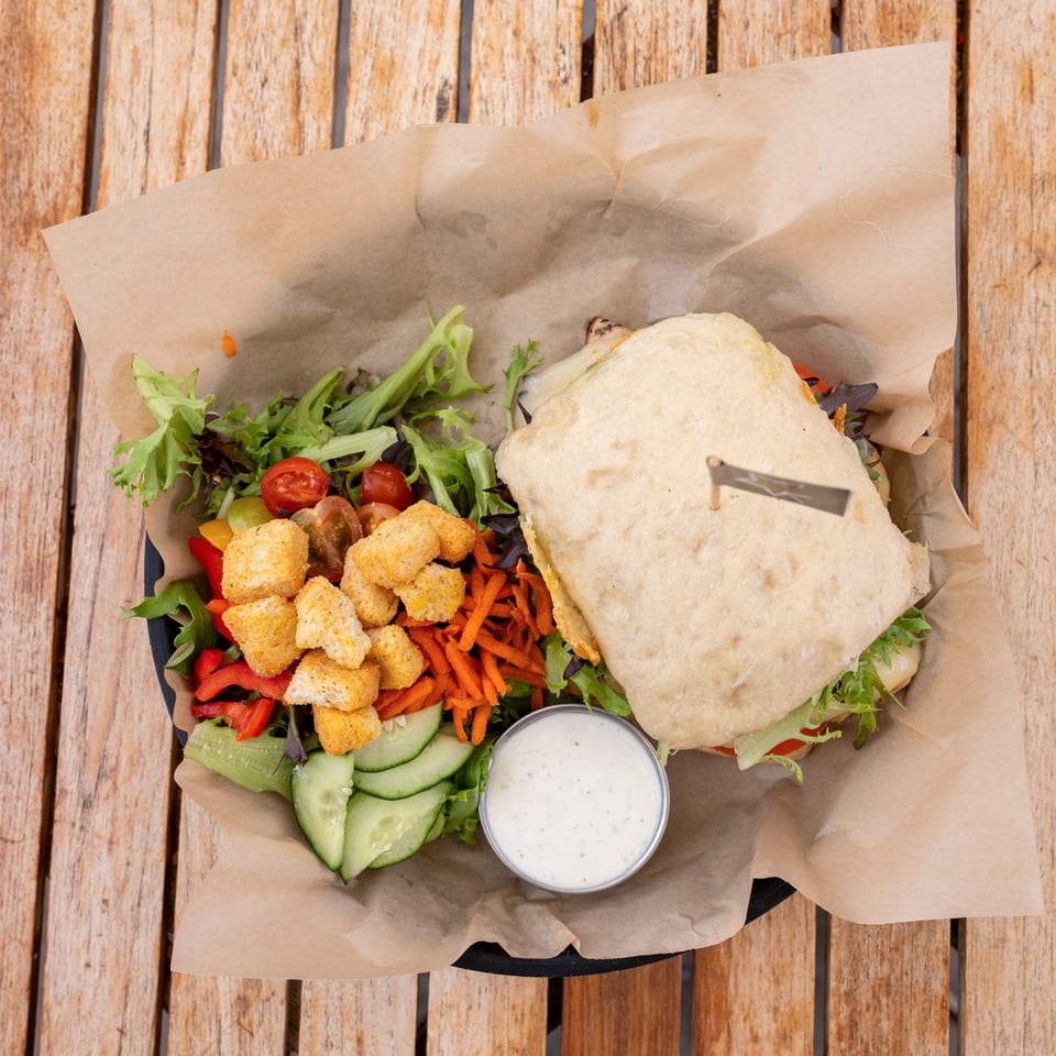 Overhead view of a sandwich and side salad with dressing, served on a wooden table.