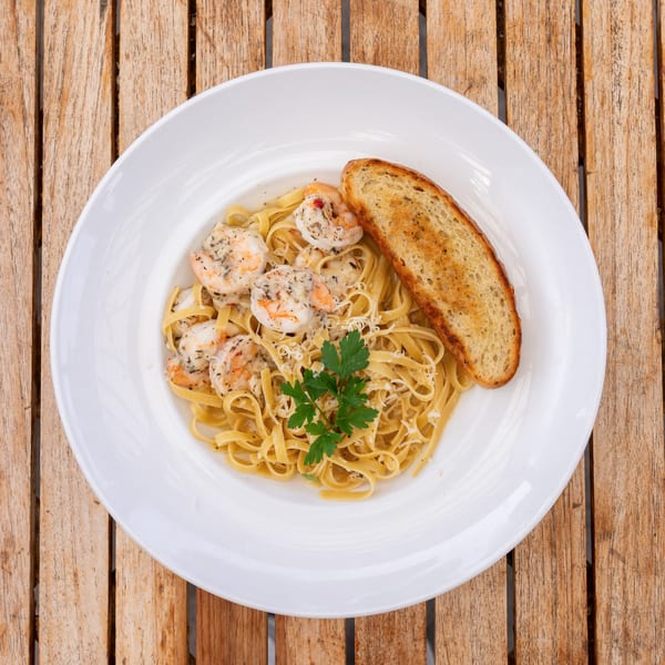 Shrimp scampi with fettuccine pasta, garlic bread, and parsley on a white plate.