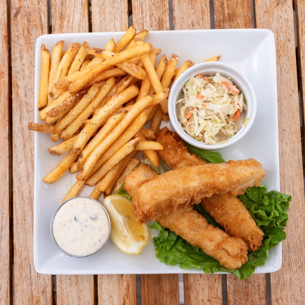 Crispy fish and chips with coleslaw, tartar sauce, and a lemon wedge on a white plate.