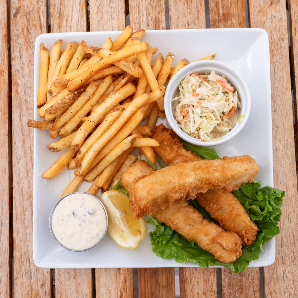 Crispy fish and chips with coleslaw, tartar sauce, and a lemon wedge on a white plate.